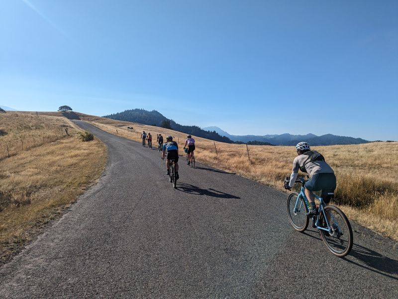 Cyclists riding up paved road with fields in the background